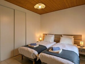 A double room with two beds, wooden headboards, bedside lamps, and a ceiling light fixture. - Le Refuge de Mazard: Comfortable nature cabin, large property, sleeps 6 (Saint-Jeures)