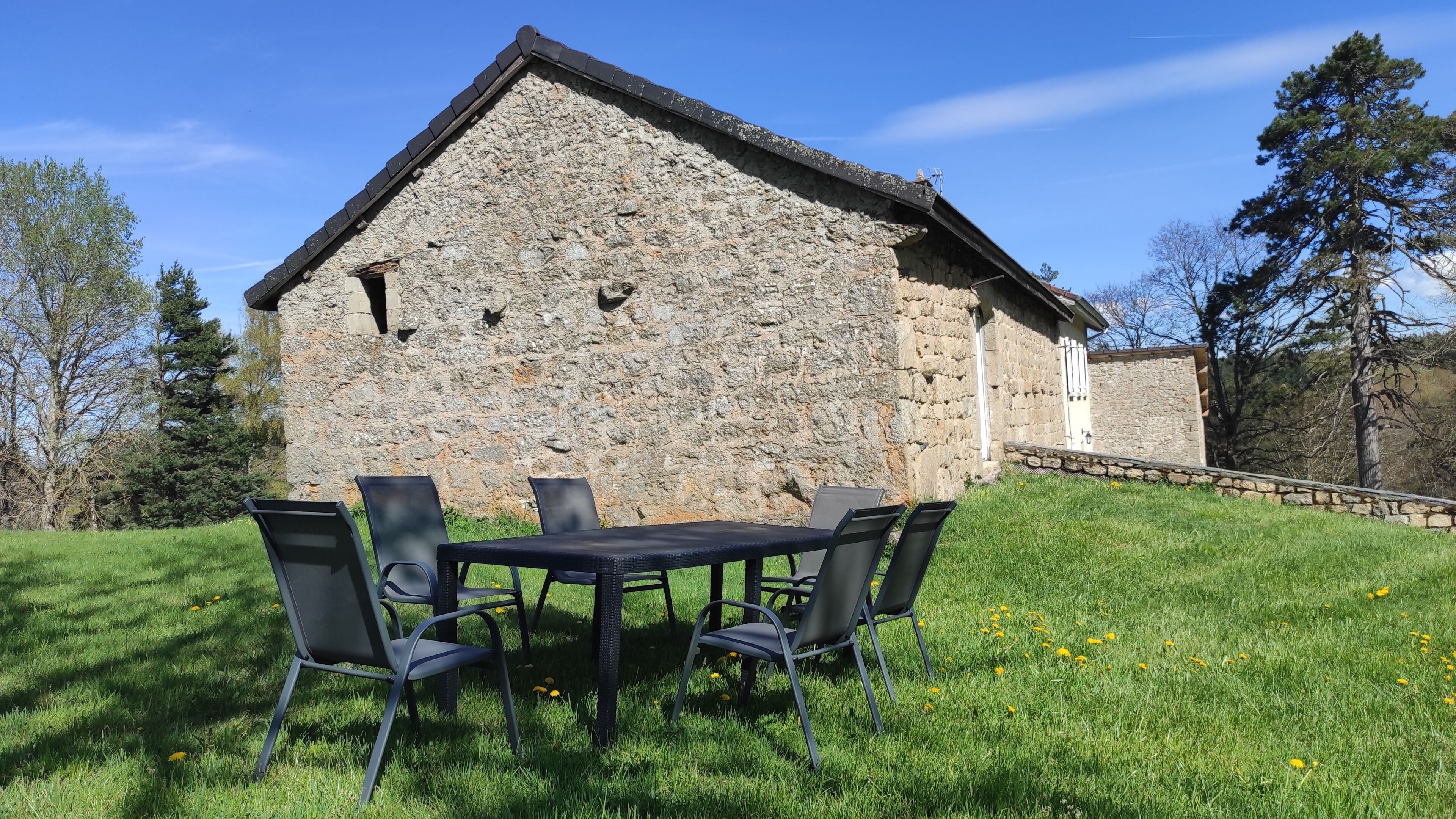 A stone building with a sloped roof, a small porch, and a grassy area with a table and chairs.