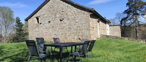A stone building with a sloped roof, a small porch, and a grassy area with a table and chairs.