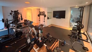 Une salle de sport à domicile équipée de matériel d’exercice, d’un grand miroir et d’un téléviseur fixé au mur.