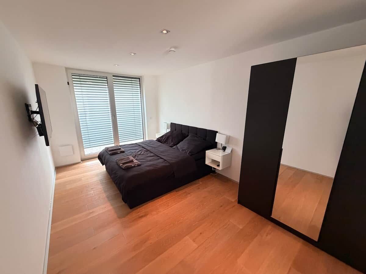 Un dormitorio con cama, mesita de noche y un espejo grande.