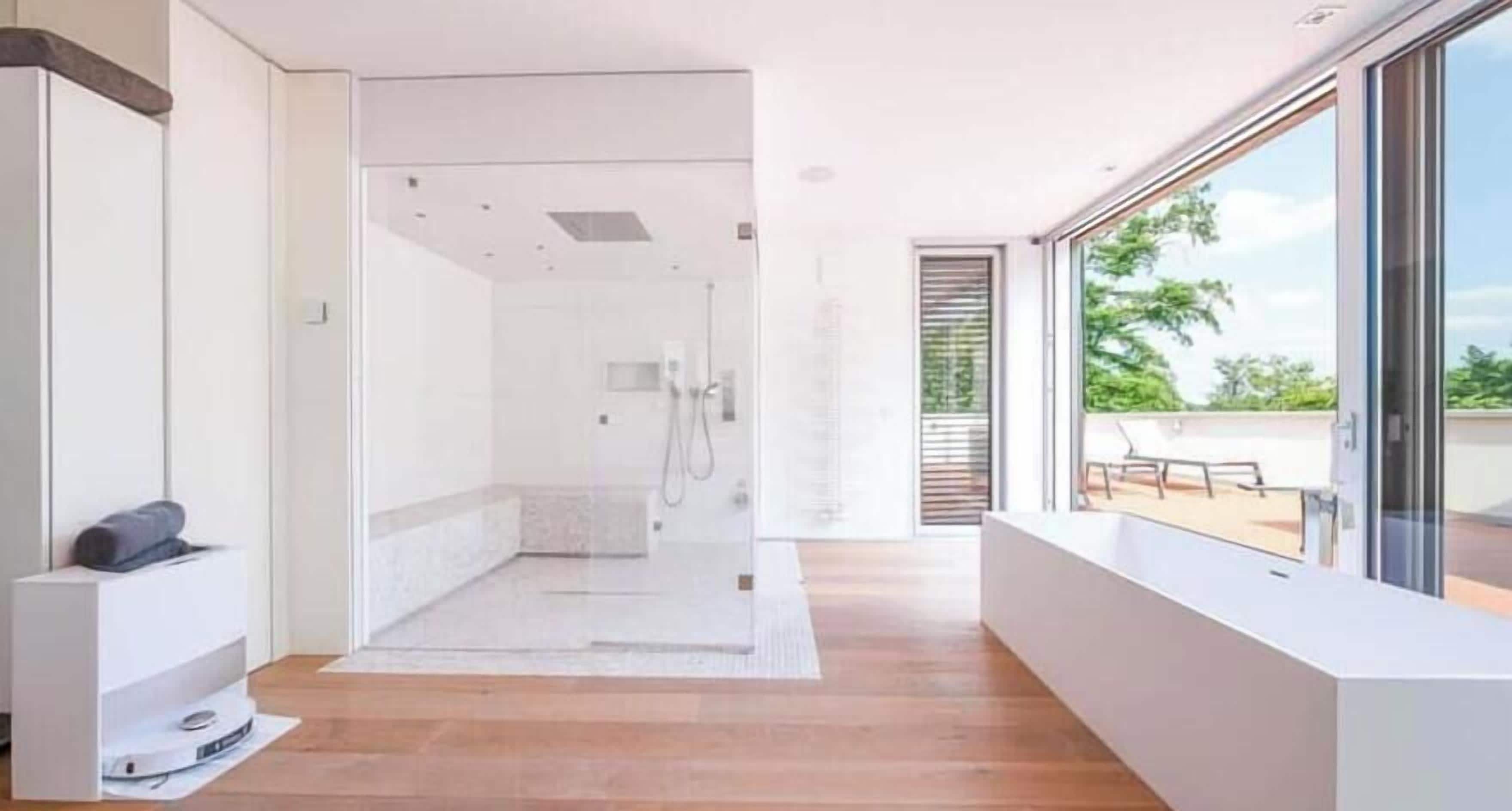 A modern bathroom with a glass shower enclosure, a wooden floor, and a view of the outdoors.