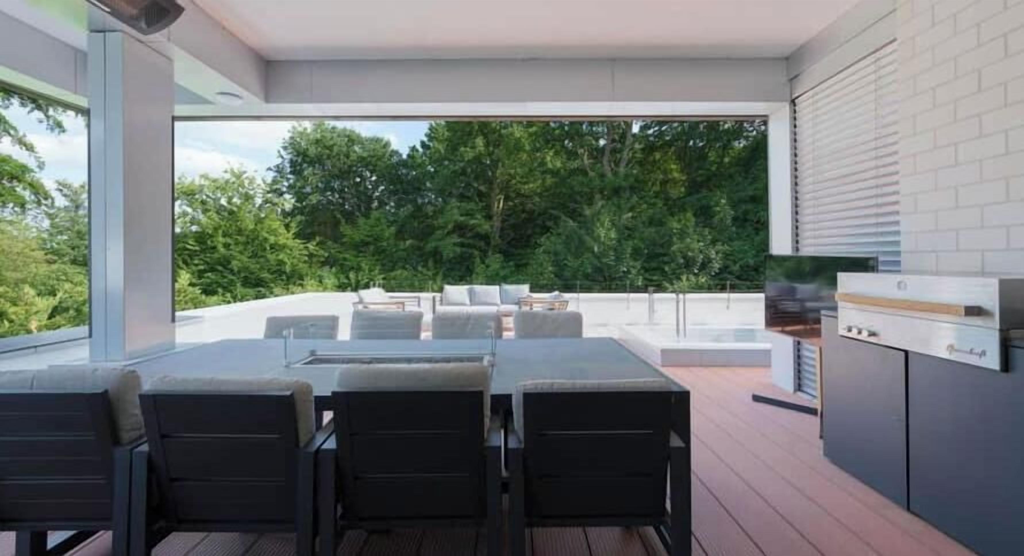 Un espacio de comedor exterior con mesa y sillas, una parrilla y vistas a árboles.