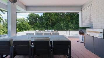 Un espacio de comedor exterior con mesa y sillas, una parrilla y vistas a árboles.