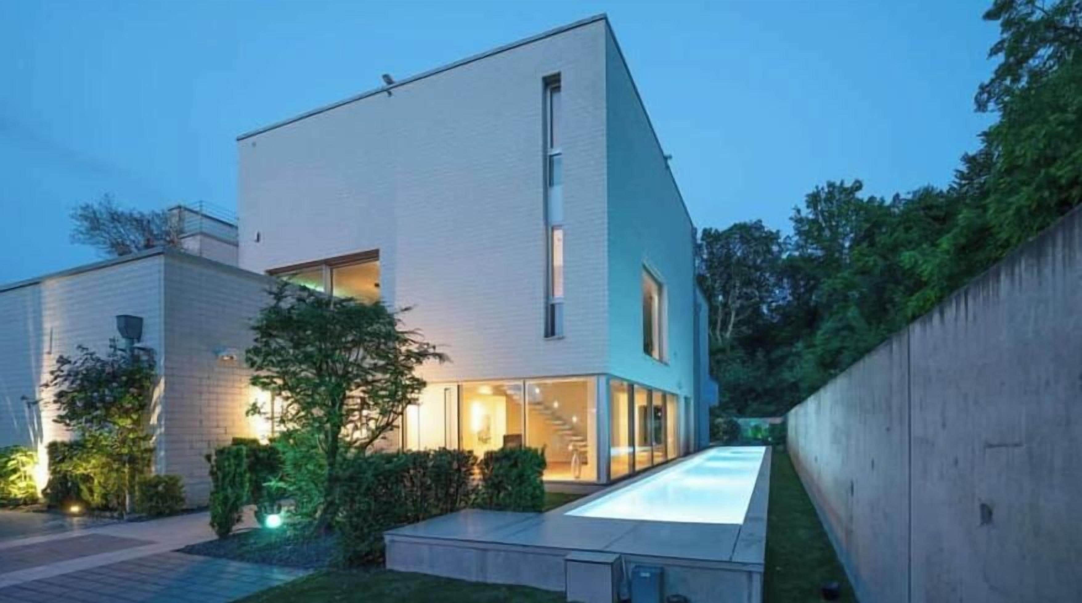 Ein modernes, zweistöckiges Gebäude mit Flachdach, großen Fenstern und einem sichtbaren Außenbereich mit einem Weg zum Eingang.