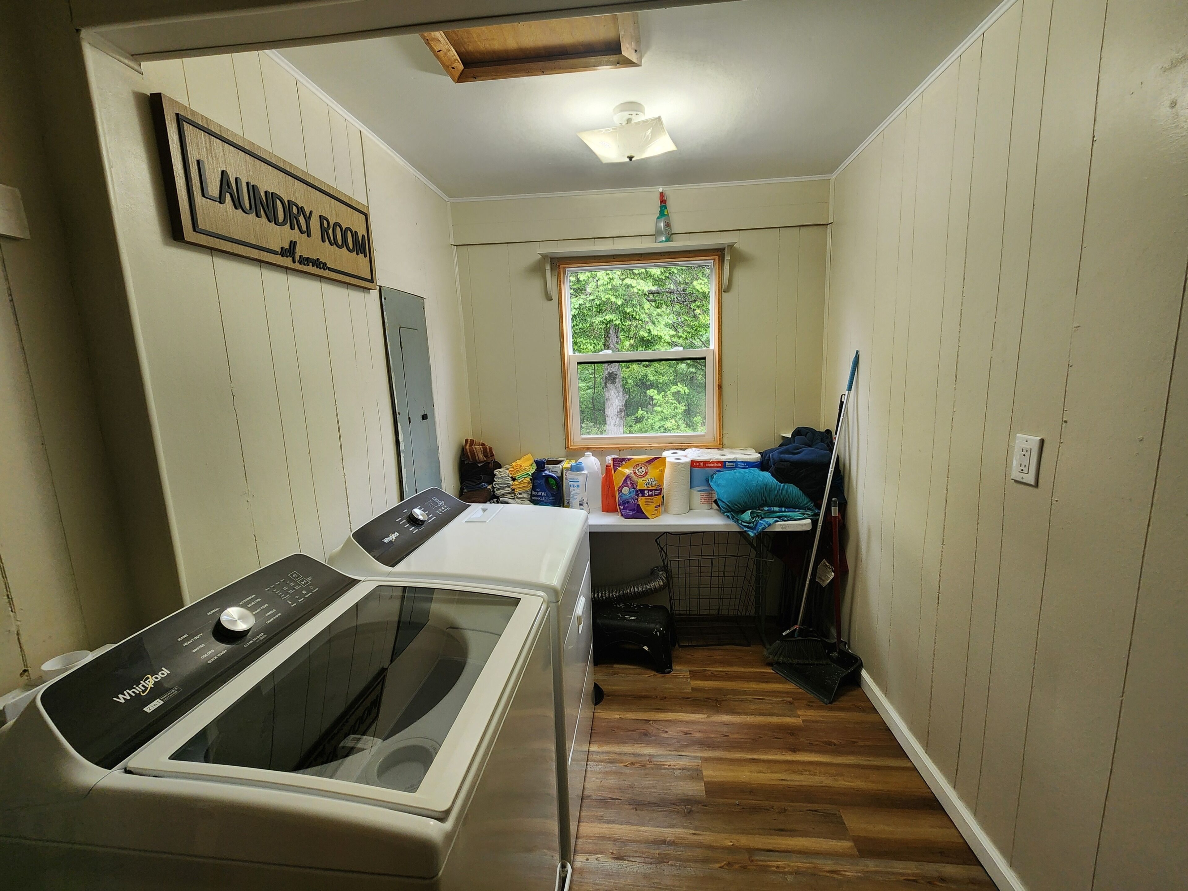 A laundry room with a Whirlpool washer, a window with a view of greenery, and a sign indicating the room's purpose.