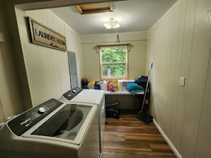 A laundry room with a Whirlpool washer, a window with a view of greenery, and a sign indicating the room's purpose.