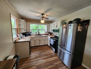 A kitchen with wooden flooring, a stainless steel refrigerator, a microwave, and a ceiling fan. - Tranquil 3-bedroom Mountain View Farmhouse in Charming Greeneville (Greeneville)