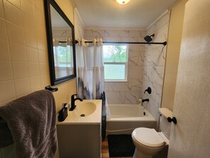 A bathroom with a sink, mirror, toilet, bathtub, and a window with a view.