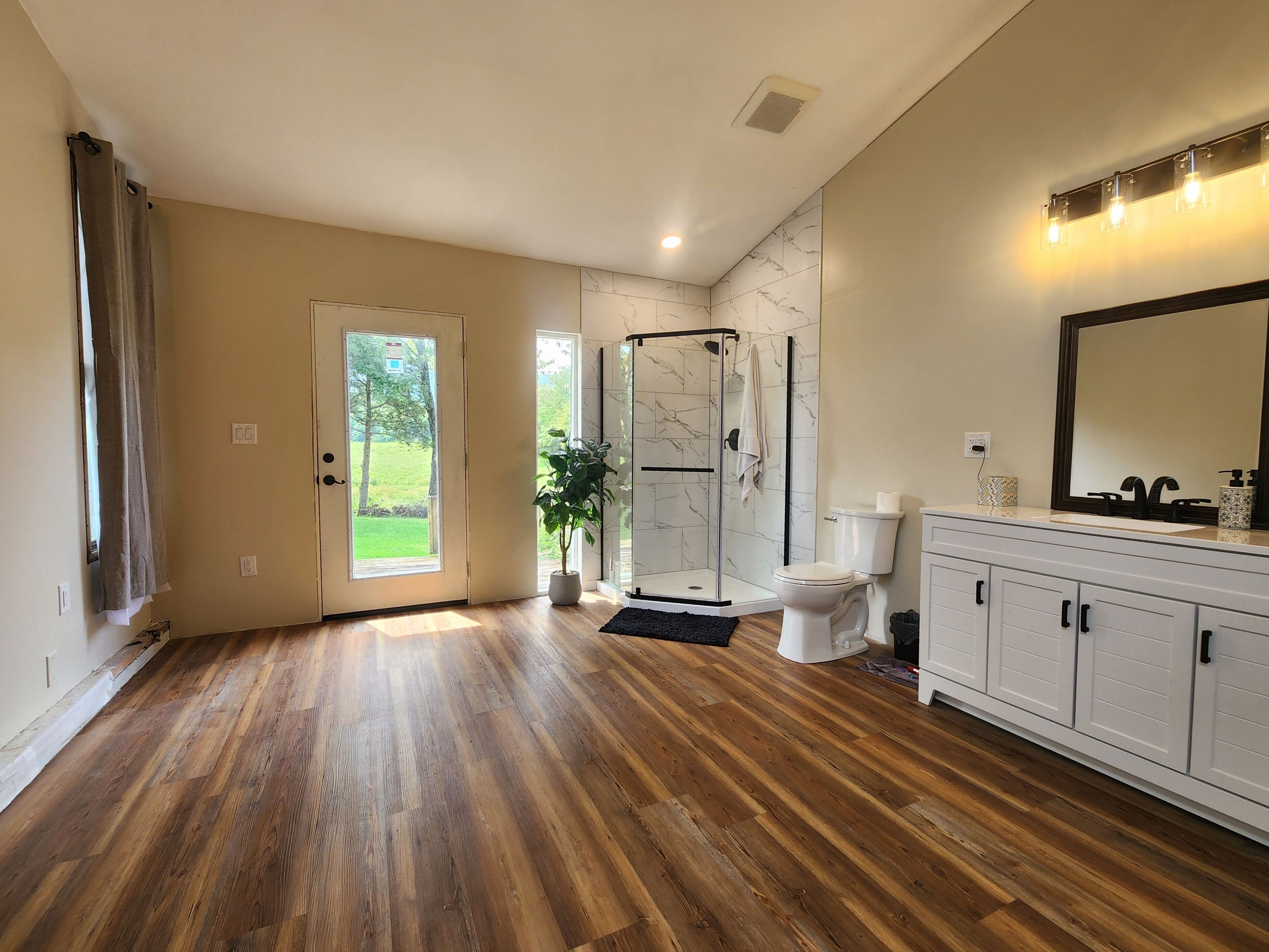 Une salle de bain spacieuse avec un plancher en bois, une douche en verre, des toilettes blanches et un meuble-lavabo avec un miroir.