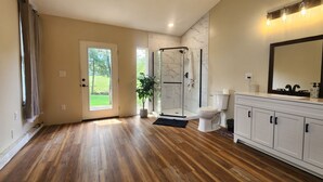Um banheiro espaçoso com piso de madeira, box de vidro, vaso sanitário branco e toucador com espelho.