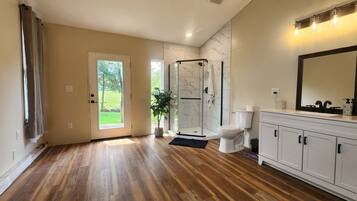 Une salle de bain spacieuse avec un plancher en bois, une douche en verre, des toilettes blanches et un meuble-lavabo avec un miroir.