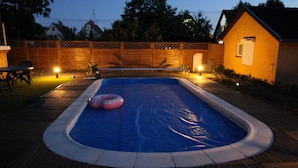 Ein rechteckiger Swimmingpool mit blauer Innenseite, umgeben von einer Holzterrasse und einer Ziegelwand.
