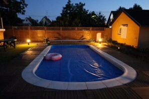 Ein rechteckiger Swimmingpool mit blauer Innenseite, umgeben von einer Holzterrasse und einer Ziegelwand.