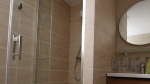 Eine Dusche mit Glastür, weißem Duschkopf und gefliesten Wänden.
