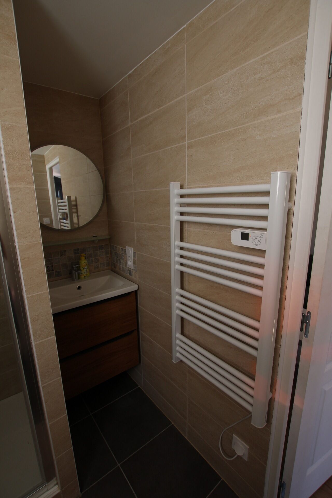 Un baño con toallero blanco, espejo y lavamanos con artículos de aseo.