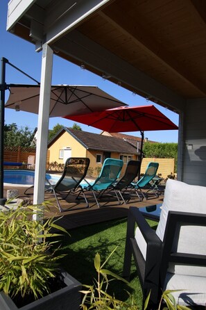 Een zwembadgedeelte met ligbedden, parasols en een huis op de achtergrond.