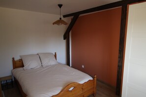 Een enkel bed met houten hoofdbord en een hangende lamp in een kamer met oranje accentmuur en een witte deur.