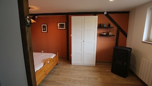 Ein Schlafzimmer mit einem hölzernen Bett, einem weißen Kleiderschrank, einem Heizgerät und einem Regal mit Küchenutensilien.