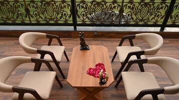 Una mesa de madera con cuatro sillas, una estatua y un arreglo de flores rojas en forma de corazón en un balcón con barandilla decorativa.