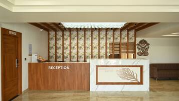 A reception desk with a wooden finish and a sign that reads 'RECEPTION.' Behind the desk, there is a patterned wall and a decorative emblem.