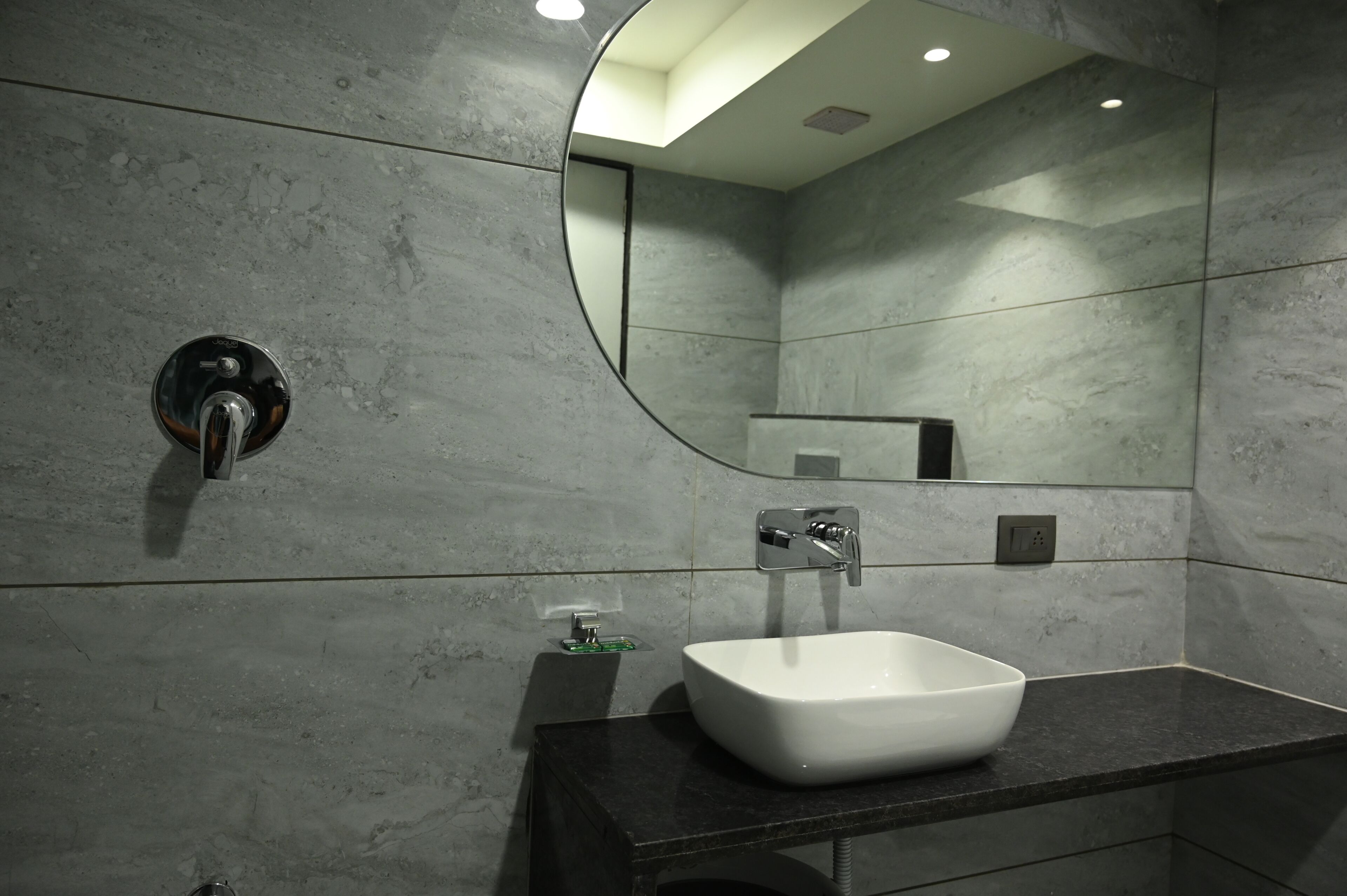 Un baño moderno con un lavabo blanco, un espejo redondo y un grifo de pared.