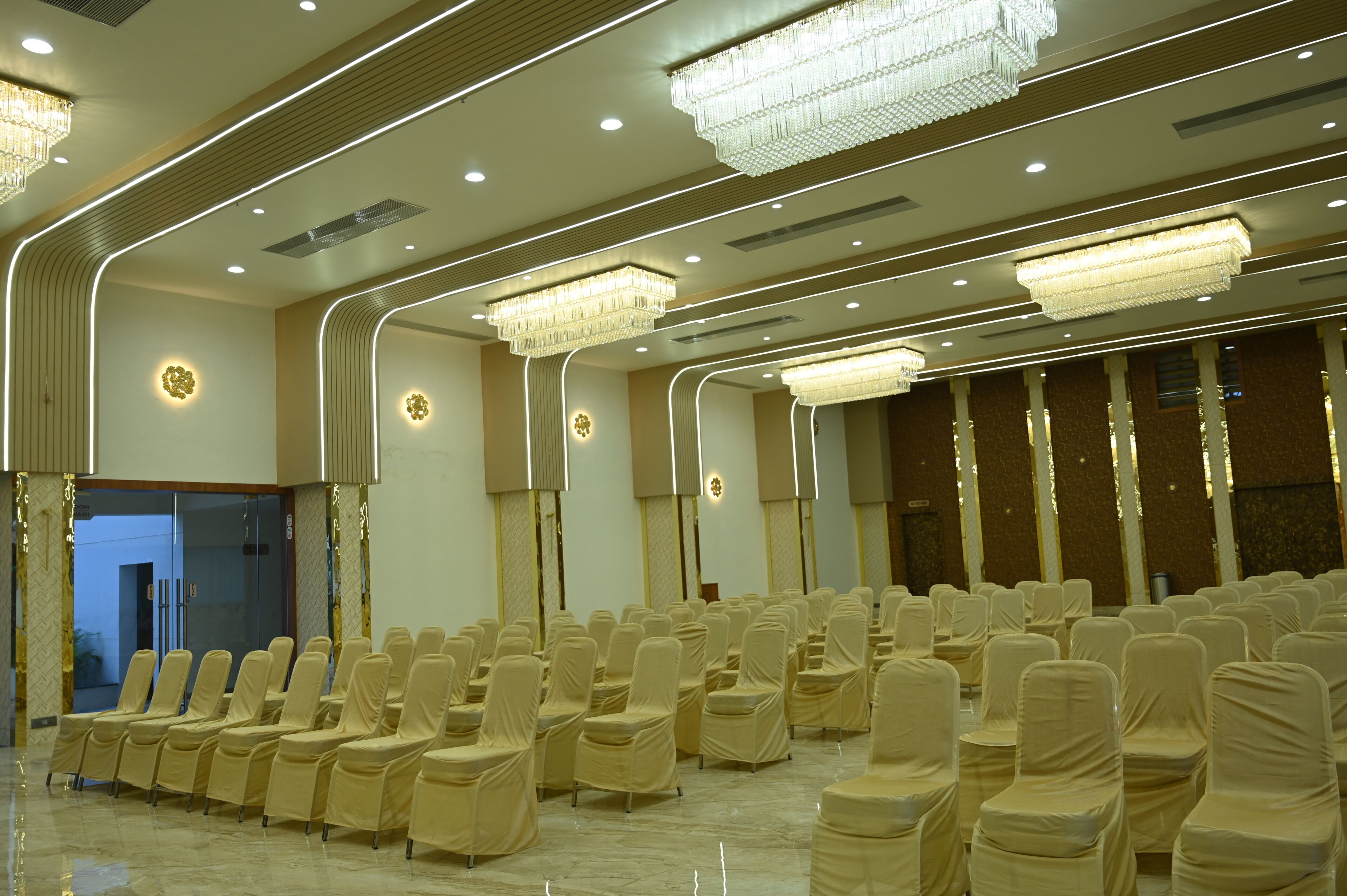 Un salón de conferencias con filas de sillas tapizadas en tela color beige, una araña y un diseño de techo moderno con iluminación empotrada.