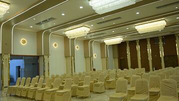 Un salón de conferencias con filas de sillas tapizadas en tela color beige, una araña y un diseño de techo moderno con iluminación empotrada.