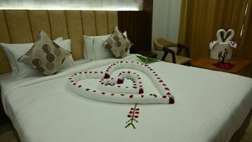 Una cama bien arreglada con un arreglo de toallas con forma de corazón, una planta decorativa y una mesita de noche con un florero y figuritas.