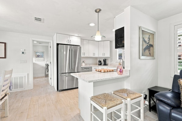 A modern kitchen with stainless steel appliances, white cabinetry, a central island with stools, and a pendant light.