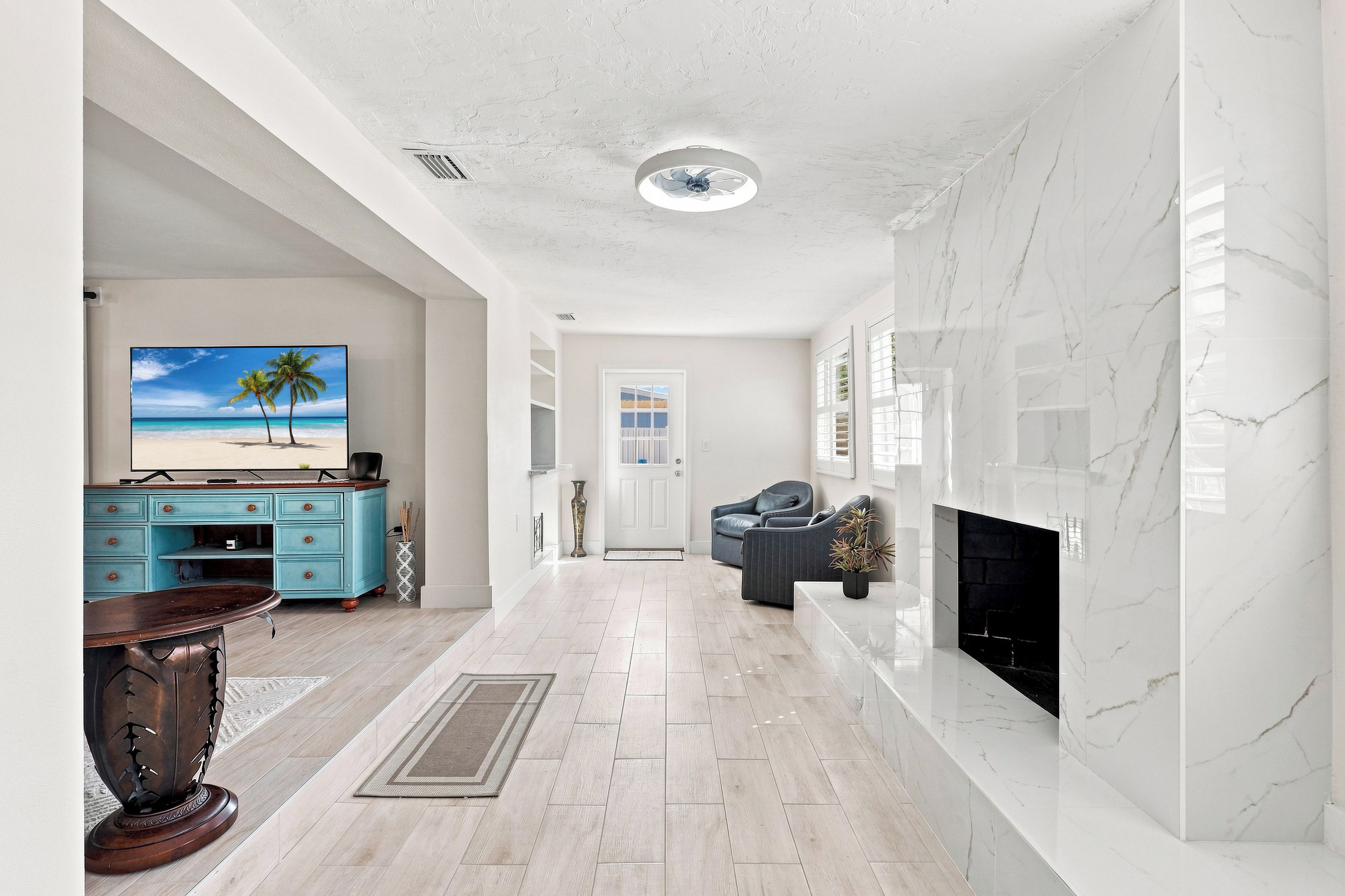 A spacious living room with a fireplace, a television, and a view of the beach through a window.