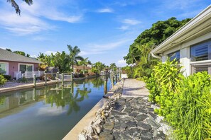 A canal with a stone walkway, houses on either side, and lush greenery.