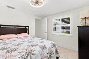 A bedroom with a bed, a window with blinds, a ceiling fan, and a nightstand.