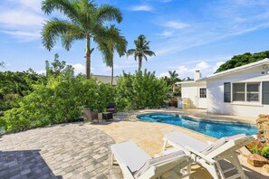 Ein Swimmingpool mit Liegestühlen, umgeben von einer Pflasterterrasse und Palmen.