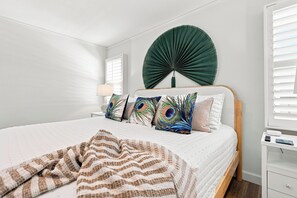 Ein ordentlich bezogenes Bett mit einer gestreiften Decke, ein Wandventilator und ein Nachttisch mit einer Lampe.