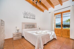 Un dormitorio con cama, mesita de noche, una obra de arte en la pared y ventana con vistas.