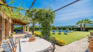 Un patio al aire libre con una mesa, sillas, una pérgola y vistas a una piscina.