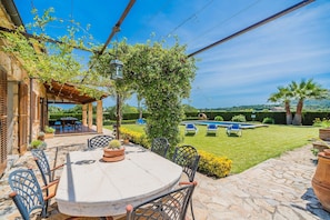 Un patio al aire libre con una mesa, sillas, una pérgola y vistas a una piscina.