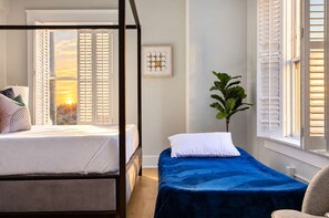 A bedroom with a bed, a bedside table, a chair, and a window with shutters. - The Penn Hotel - Steps to Gaslamp & Petco Park, AC (San Diego)