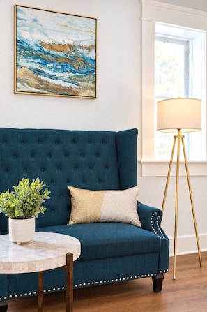 A blue sofa with a tufted backrest, a round table with a potted plant, and a floor lamp with a gold base. - The Penn Hotel - Smart TV, AC & Gaslamp Steps Away (San Diego)