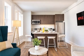 A modern kitchen with a central island, stainless steel appliances, and bar stools. - The Penn Hotel - Smart TV, AC & Gaslamp Steps Away (San Diego)