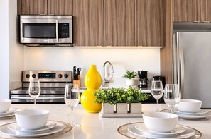 A modern kitchen with stainless steel appliances, a yellow vase, and a plant on the counter. - The Penn Hotel - Smart TV, AC & Gaslamp Steps Away (San Diego)
