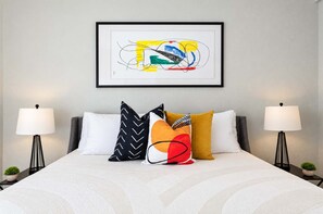 A neatly made bed with a white comforter, multiple pillows in various patterns, and two bedside lamps on either side. - The Penn Hotel - Smart TV, AC & Walk to Gaslamp!!! (San Diego)