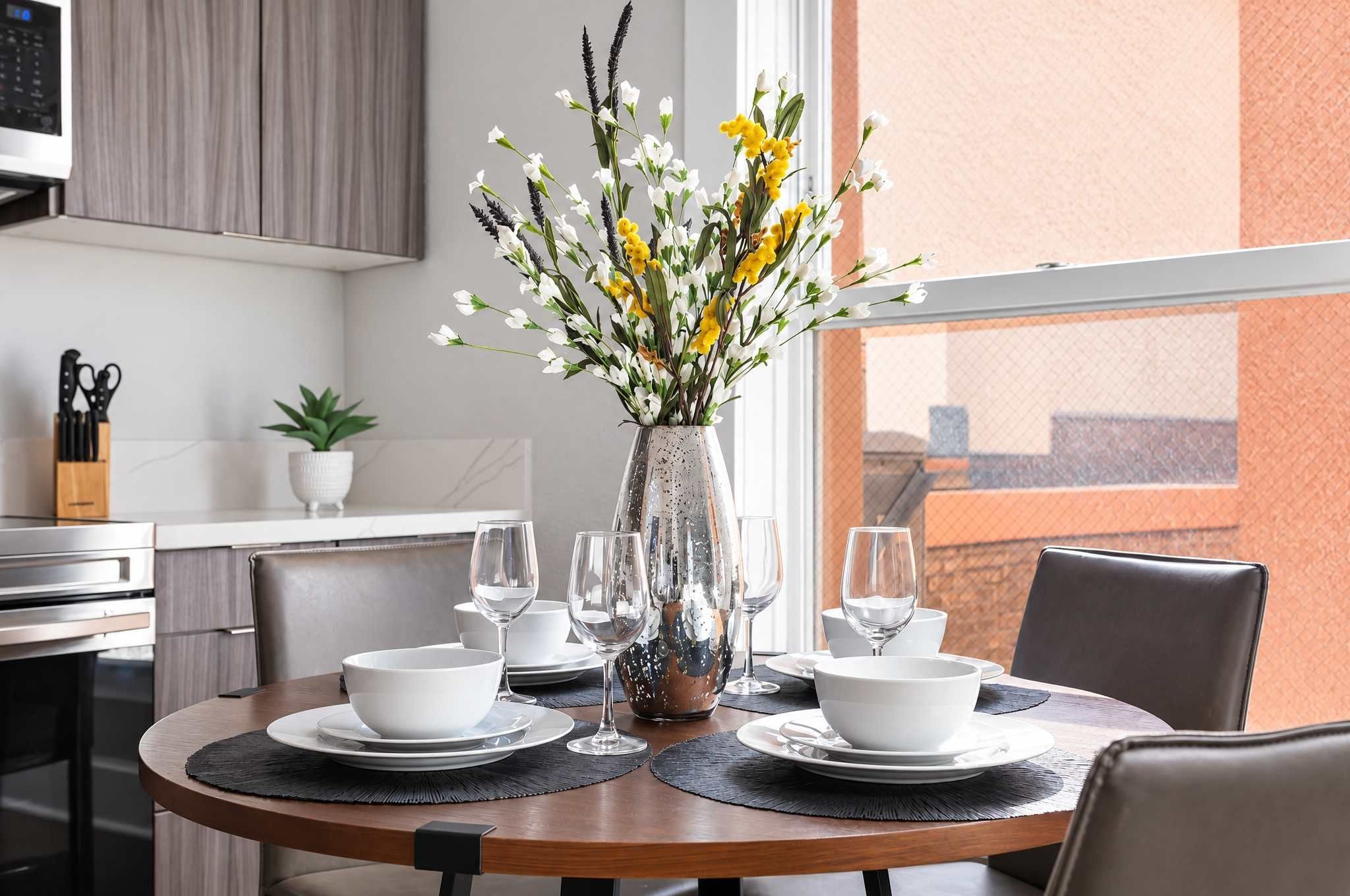 A dining table set with white bowls, wine glasses, and a vase with flowers.