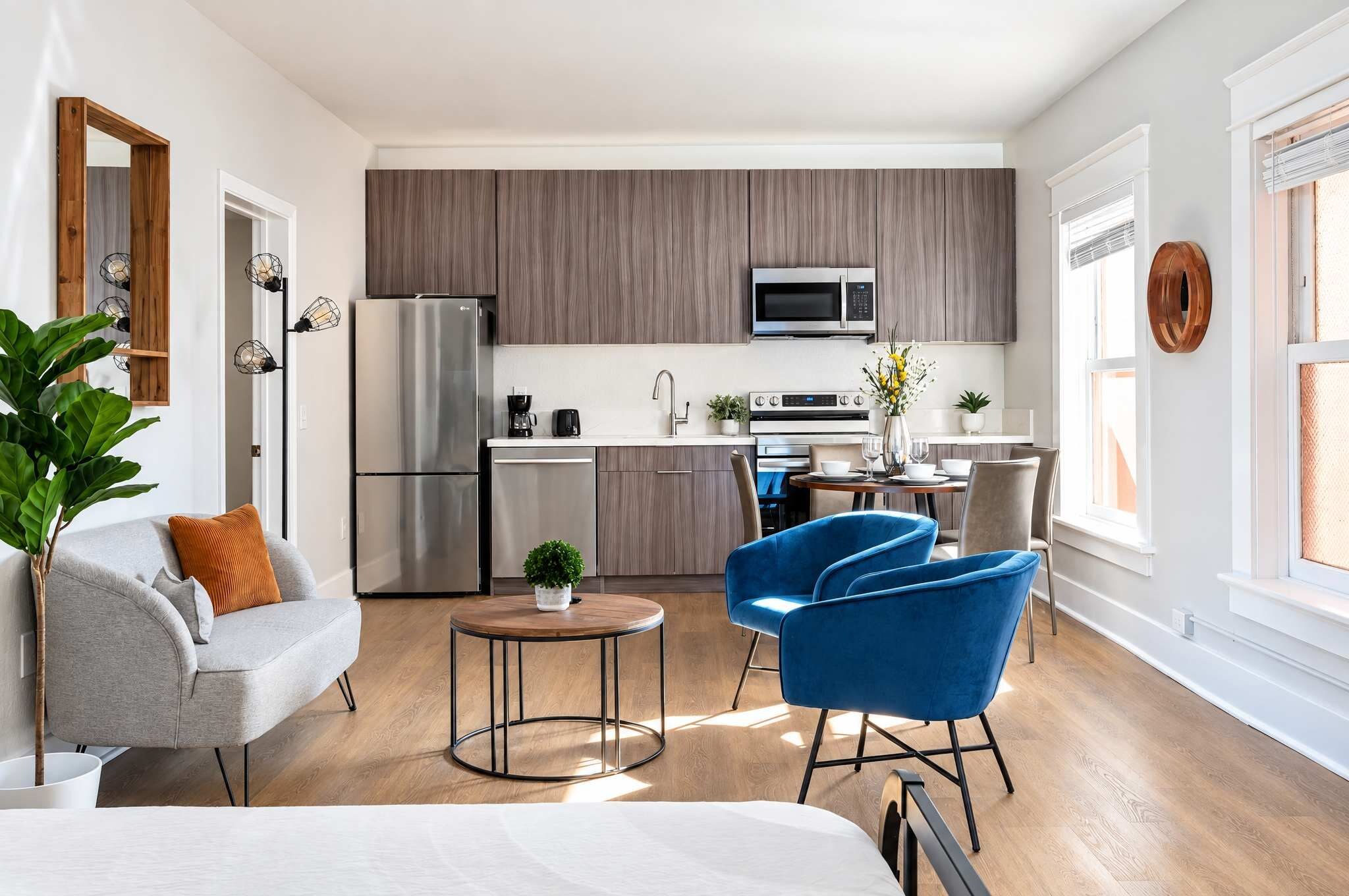 A modern kitchen with a built-in microwave, a refrigerator, and a dining area with a blue chair and a small round table.