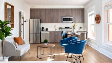 A modern kitchen with a built-in microwave, a refrigerator, and a dining area with a blue chair and a small round table.
