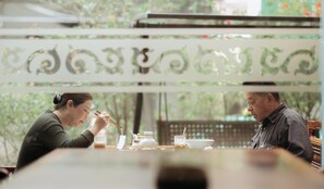 Una mesa de comedor con diversos platos y utensilios, un biombo decorativo con un diseño, y un fondo natural al aire libre.