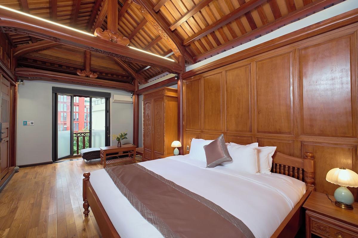 A hotel room with a large bed, wooden headboard, and a balcony with a view of buildings.