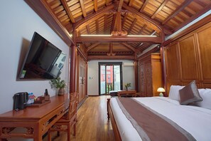 A hotel room with a wooden ceiling, a bed, a TV on the wall, and a desk with a vase of flowers. - Thong Dong Quan Boutique Hotel Hue (Thuan Hoa)