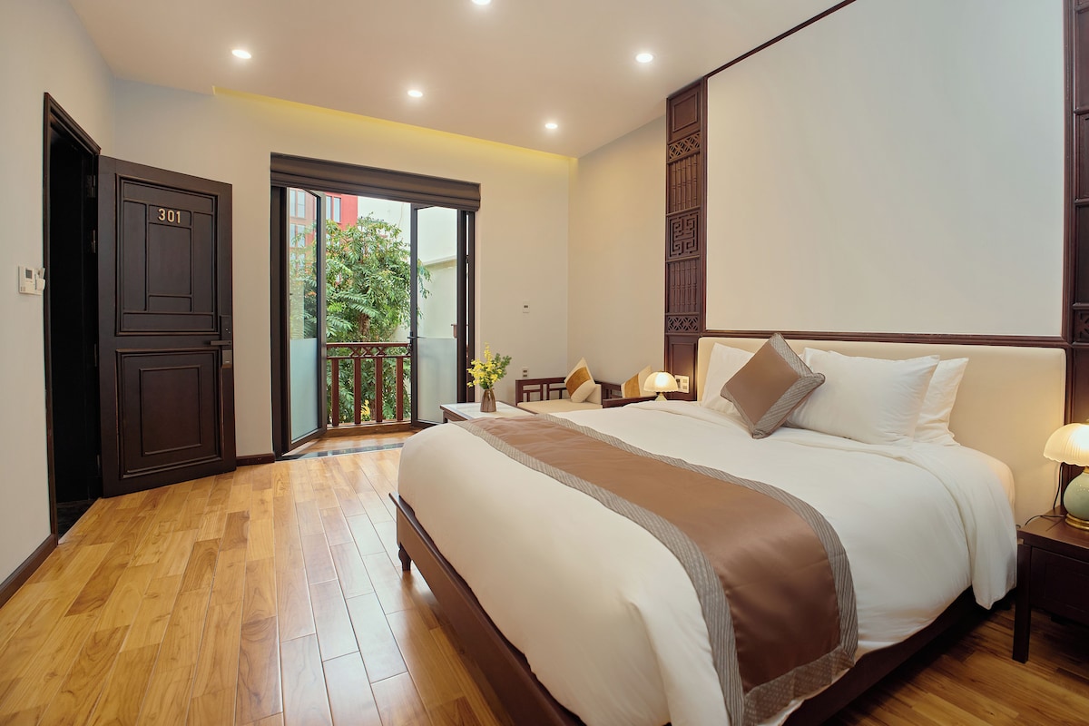 A hotel room with a large bed, a balcony, and a wooden floor.